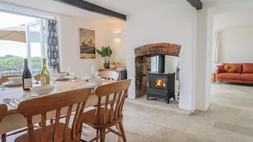 A dining area with a table set for two, a brick fireplace, and a sofa in the background.