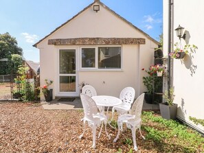 Ein Gebäude mit einer steinverzierten Eingangspforte, heller Fassade und einer kleinen Terrasse mit rundem Tisch und Stühlen.