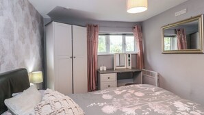 Ein Schlafzimmer mit Bett, Schreibtisch, Kleiderschrank, Spiegel und einem fenster mit Vorhängen.