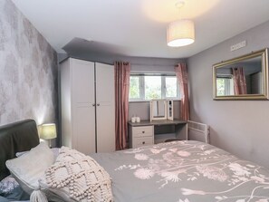 Ein Schlafzimmer mit Bett, Schreibtisch, Kleiderschrank, Spiegel und einem fenster mit Vorhängen.