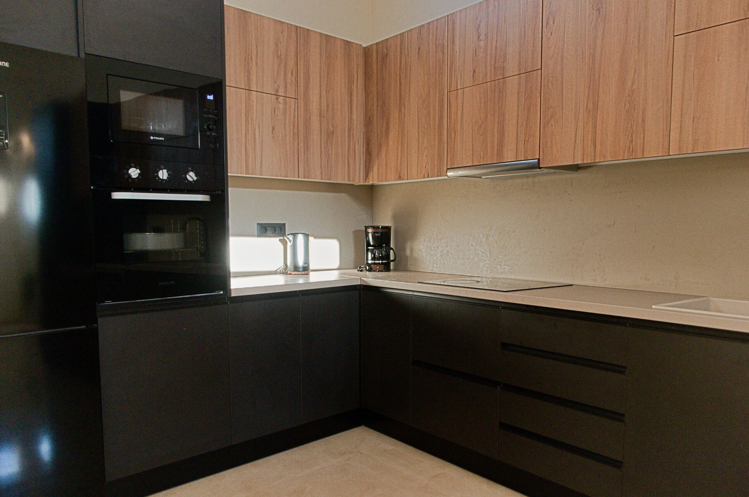 A kitchen with dark cabinetry, a built-in oven, a coffee maker, and a window.