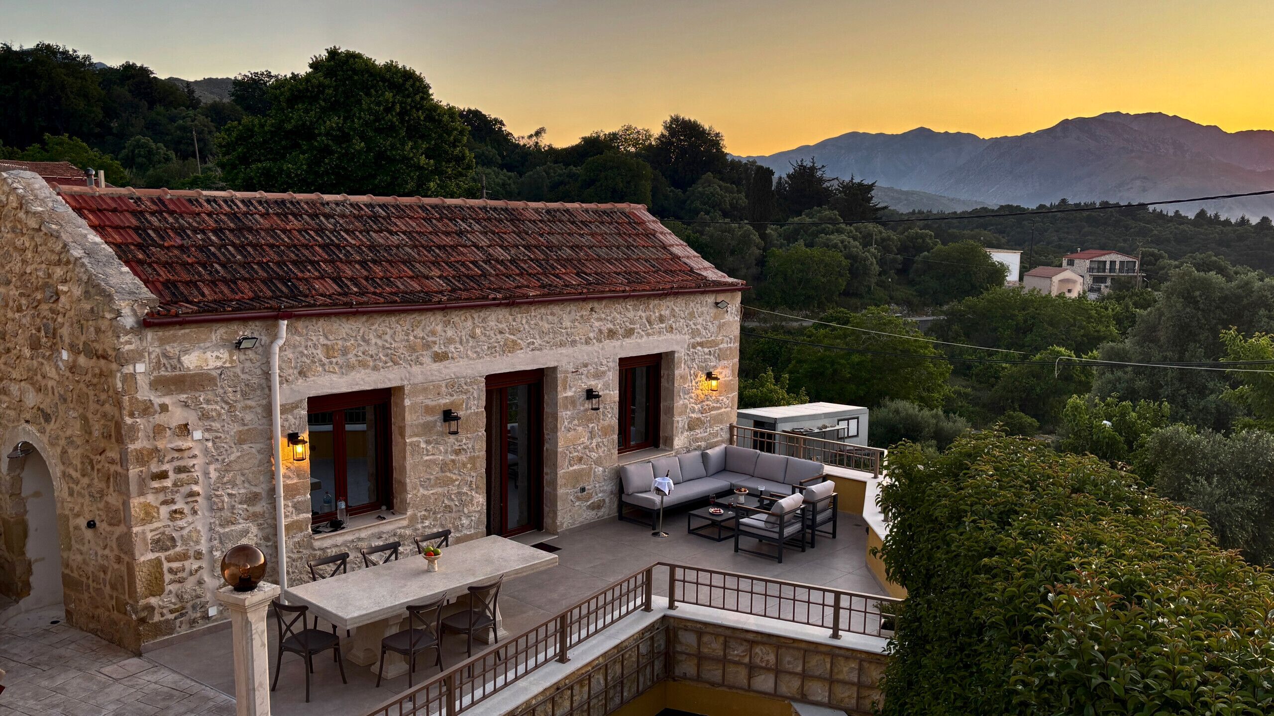 Un edificio de piedra con terraza, mobiliario exterior y vistas a las montañas.