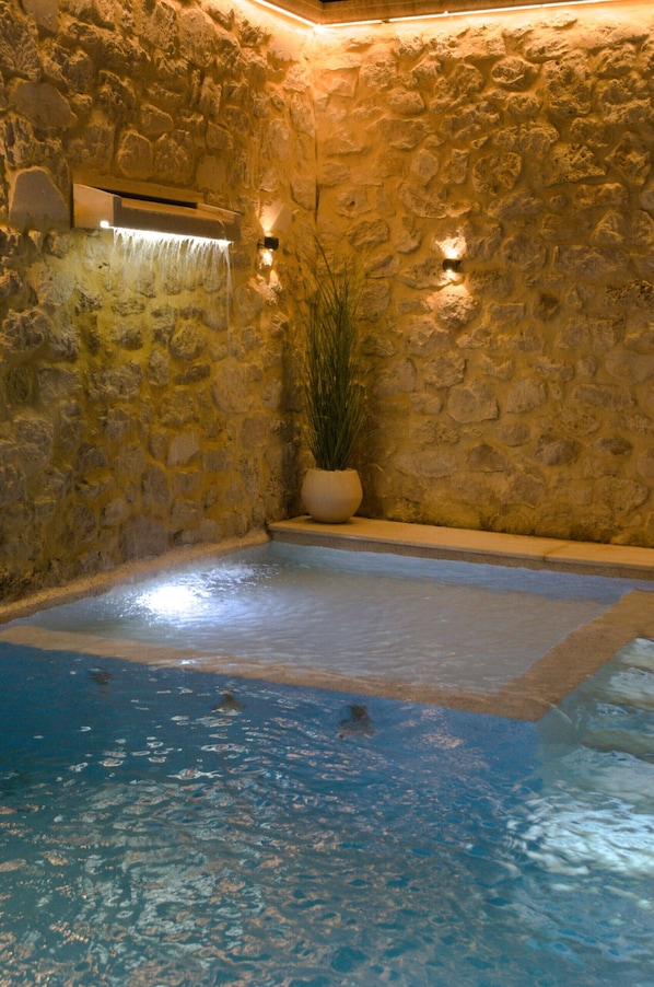 Ein Innenpool mit Steinwänden, klarem Wasser, einer Topfpflanze und Wandleuchten.
