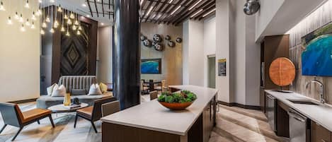 A modern hotel lobby with a central island, seating area, and a large TV.