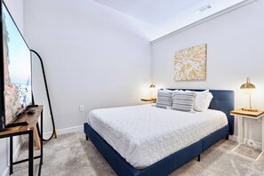 Ein Schlafzimmer mit Bett, Fernseher, zwei Nachttischlampen, einem Bild und Teppichboden.