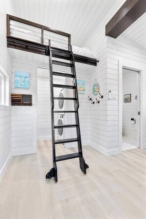 Ein Zimmer mit einer schwarzen Metallleiter an einer weißen, vertikalen Wand, einer Waschmaschine und einer Tür zu einem weiteren Raum.