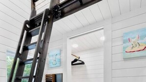 A room with white paneled walls, a wooden ladder, a painting, a TV, and a wooden cabinet. - Modern Retreat|Tiny House|Weekly&Monthly Discount (Richardson)