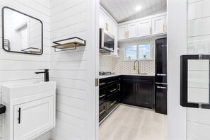 A modern kitchen with white cabinetry, a black refrigerator, and a window with a view. - Modern Retreat|Tiny House|Weekly&Monthly Discount (Richardson)