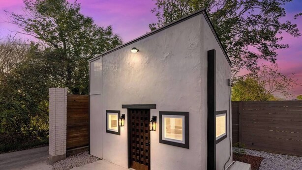 A modern single-story building with a flat roof, a wooden door, and two wall-mounted light fixtures. - Modern Retreat|Tiny House|Weekly&Monthly Discount (Richardson)