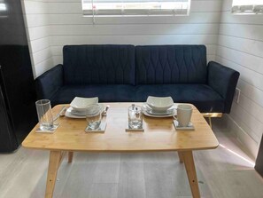 A dining table set with plates, glasses, and cutlery in a room with a dark blue sofa and light-colored walls. - Modern Retreat|Tiny House|Weekly&Monthly Discount (Richardson)