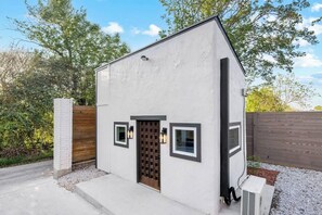 A small, single-story building with a white exterior, a wooden door, and two small windows. - Modern Retreat|Tiny House|Weekly&Monthly Discount (Richardson)