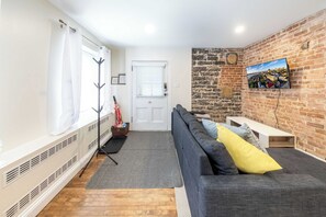 Een woonkamer met een bank, een televisie bevestigd aan een bakstenen muur, een witte deur en een radiator.