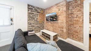 Una habitación con pared de ladrillo, televisor montado, sofá y una puerta.