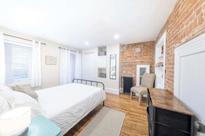 A bedroom with a bed, a chair, a desk, a radiator, and a brick wall. - Near the Ferry | L'Appartement des Notaires (Lévis)