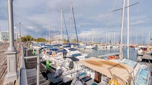 Un port esportiu amb embarcacions amarrades, una passera de fusta i un paisatge urbà al fons.