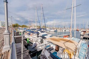 A marina with boats docked, a wooden walkway, and a cityscape in the background. - 2BR Sunrise Port View Apt Steps from Finikoudes (Larnaka)
