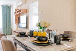 A dining table set with black and yellow plates, a vase with white flowers, and a television in the background. - 2BR Sunrise Port View Apt Steps from Finikoudes (Larnaka)