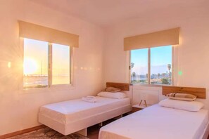 A room with two single beds, a window with a view, and a radiator. - 2BR Sunrise Port View Apt Steps from Finikoudes (Larnaka)