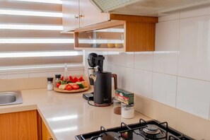 Eine Küche mit Gaskochfeld, einer Kaffeemaschine, einem Schneidebrett mit Gemüse und einem Gewürzregal.