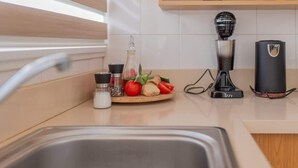 Eine Küche mit Spüle aus Edelstahl, einem Holztisch mit Tomaten und Kräutern, einer Kaffeemaschine und einer Flasche Olivenöl.