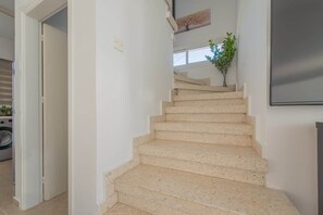 Eine Treppe mit beigen Stufen führt zu einer Empore, auf der sich ein Blumentopf befindet. Darüber an der Wand hängt ein Kunstwerk.