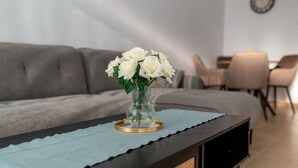 Ein Wohnzimmer mit einer Couch, einem Couchtisch mit einer Vase weißer Blumen und einem Essbereich mit Stühlen und einem Tisch.