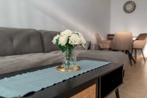 A living room with a sofa, a coffee table with a vase of white flowers, and a dining area with chairs and a table. - 3BR Sunset View Retreat Steps from the Beach (Oroklini)