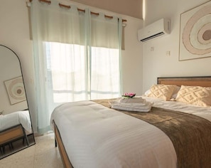 A hotel room with a bed, a chair, a mirror, and a window with curtains. - 3BR Sunset View Retreat Steps from the Beach (Oroklini)
