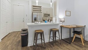 Una cocina moderna con una isla central, taburetes de bar, una mesa de comedor y un cubo de basura.