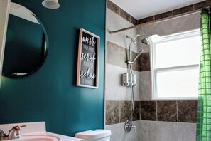 A bathroom with a teal wall, a framed sign, a shower, and a window with a green curtain. - New Listing! 1 Bed 1 Bath ny UC/OTR! (Cincinnati)