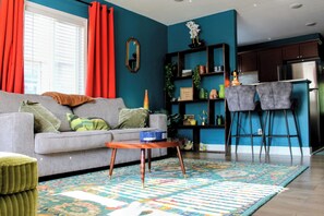 A living room with a sofa, a coffee table, a rug, and a kitchen area with a fridge and bar stools. - New Listing! 1 Bed 1 Bath ny UC/OTR! (Cincinnati)