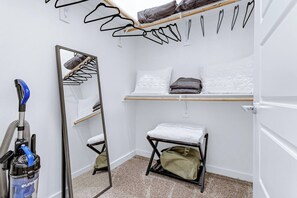 A compact hotel room with a mirror, a small bench, a shelf with pillows, and a vacuum cleaner. - Quiet Getaway | Weekly & Monthly Discounts (Richardson)
