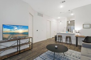 A modern living room with a flat-screen TV, a small round table, and a patterned rug. - Relax & Save | Weekly & Monthly Discounts (Richardson)