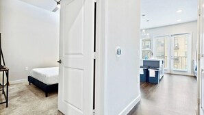 Ein Schlafzimmer mit einem Bett, einem Deckenventilator und einer Tür zu einem Badezimmer mit Waschbecken und Fenster.