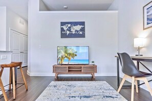 Ein Wohnzimmer mit Fernseher auf Holzfuß, einer Weltkarte darüber und einer Strandansicht auf dem Bildschirm.