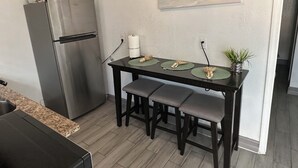 A compact kitchen with a refrigerator, a dining table with four chairs, and a painting on the wall. - Cozy 1-bedroom studio 1bath Orlando with Jacuzzi (Orlando)
