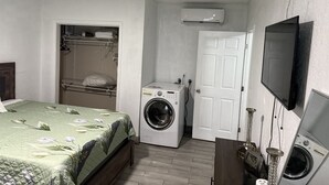 A bedroom with a bed, a washing machine, a TV, and a door. - Cozy 1-bedroom studio 1bath Orlando with Jacuzzi (Orlando)