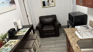 A compact kitchen with a dining area, a black leather chair, a microwave, and a granite countertop. - Cozy 1-bedroom studio 1bath Orlando with Jacuzzi (Orlando)