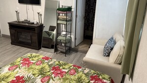 A bedroom with a bed, a TV, a dresser, a mirror, a shelf with folded towels, and a door leading to another room. - Cozy 1-bedroom studio 1bath Orlando with Jacuzzi (Orlando)