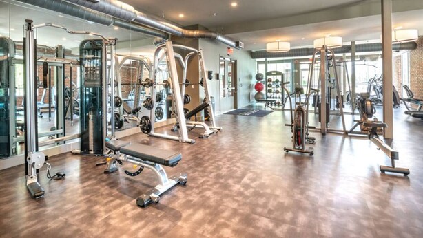 A gym with various exercise equipment, mirrors, and a wooden floor. - Near Trails & Eats | Weekly & Monthly Specials (Richardson)