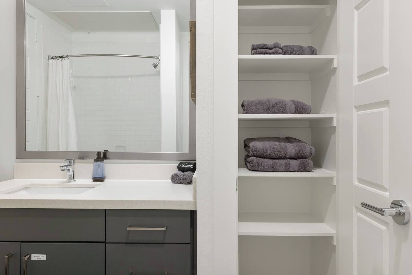 A bathroom with a white sink, a mirror, a towel rack, and a shelf with folded towels.