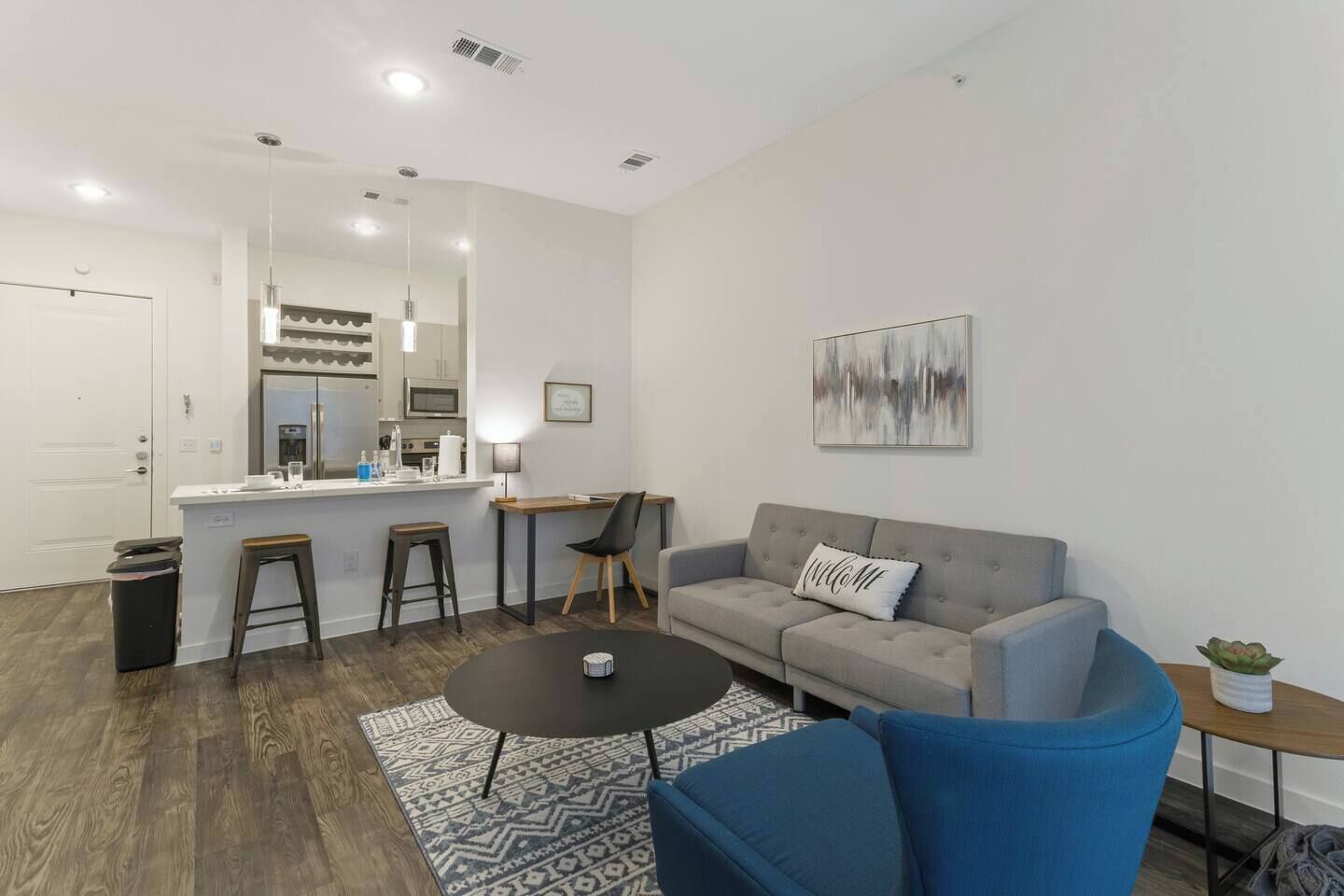 A modern living room with a grey sofa, a blue armchair, a coffee table, and a kitchen area with a bar counter.