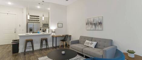 A modern living room with a grey sofa, a blue armchair, a coffee table, and a kitchen area with a bar counter.