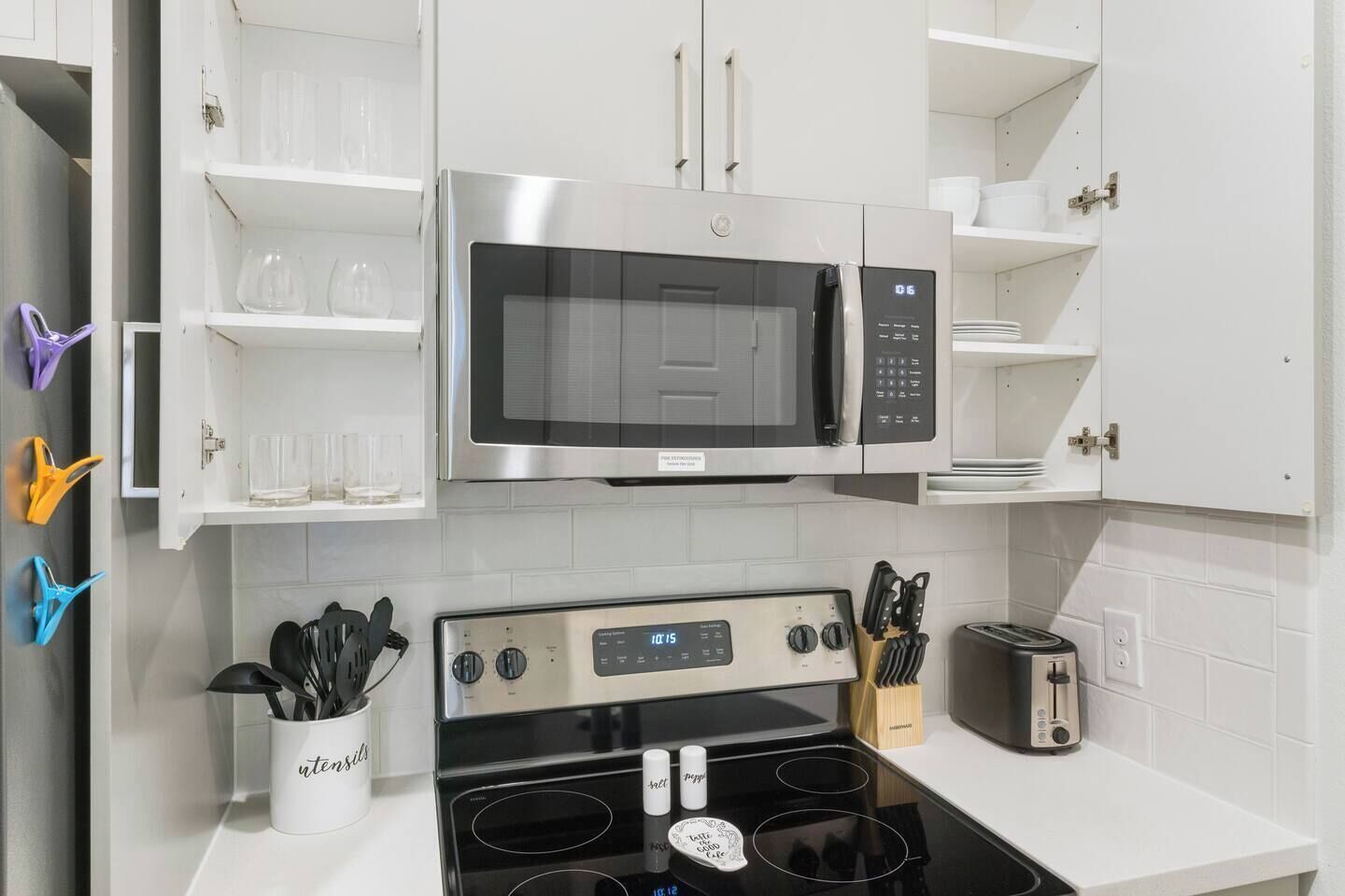 A modern kitchen with white cabinetry, a stainless steel microwave, a gas stove, and various kitchen utensils.