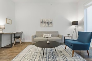 A living room with a sofa, a blue armchair, a coffee table, a floor lamp, a side table, and a rug. - Near Trails & Eats | Weekly & Monthly Specials (Richardson)