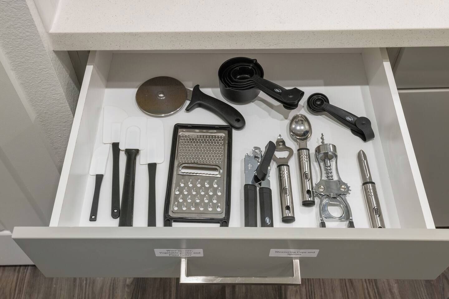 Een lade gevuld met verschillende keukengerei en benodigdheden, zoals een rasp, maatbekers en een kurkentrekker.