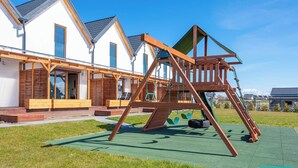 A wooden swing set in a grassy area with a row of white houses in the background. - Pleasant 2-bedroom house with AC in charming Mielenko (Mielenko)