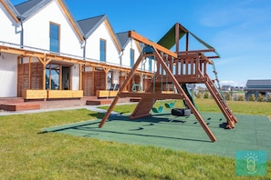 A wooden swing set in a grassy area with a row of white houses in the background. - Pleasant 2-bedroom house with AC in charming Mielenko (Mielenko)