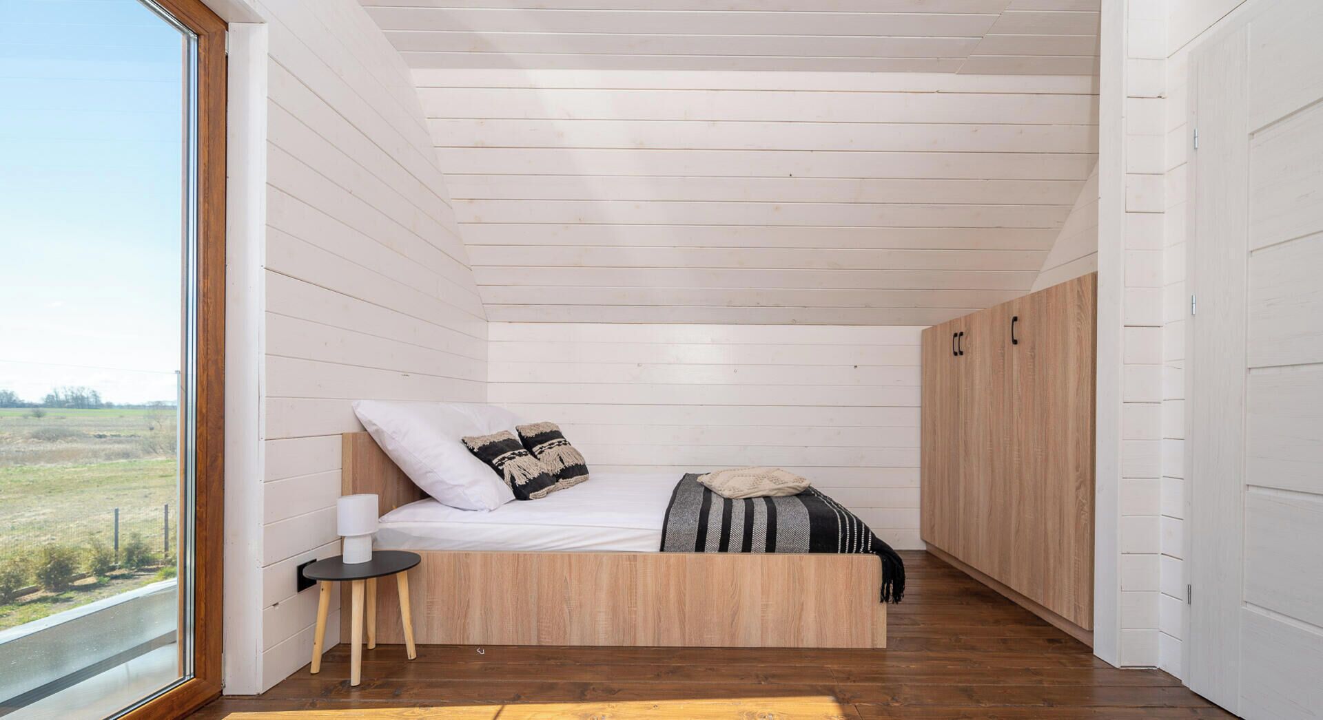 A bedroom with a wooden bed, a small bedside table, and a view of the outdoors.