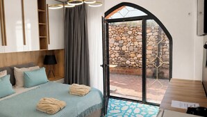 A bedroom with a bed, bedside table, lamp, and a view of a stone wall through a glass door. - Citadel 360 Suites & Spa (Skopje)